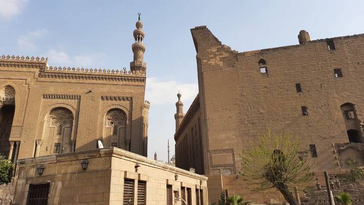 Two adjoining historic buildings and minarets rise above old Cairo streets.