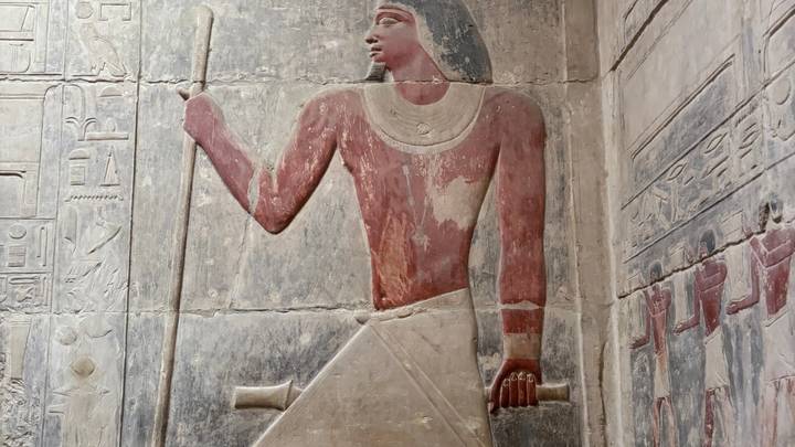 Ancient painted relief of an Egyptian noble holding a staff inside a tomb.