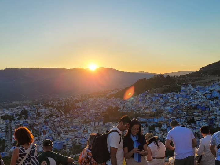 Sun setting behind mountains overlooking the blue city of Chefchaouen crowded with visitors.