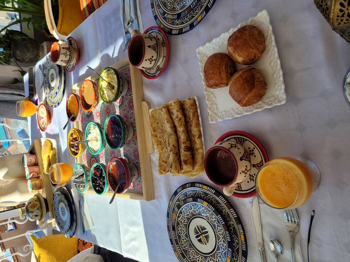 Colorful Moroccan breakfast spread on an outdoor table with assorted breads, pastries, dips and fresh juice in bright morning light.