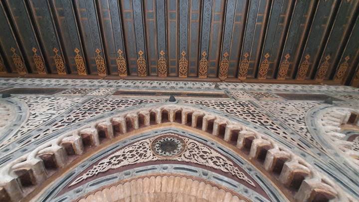 Detailed interior stone archway and patterned ceiling with intricate Islamic geometric carvings.
