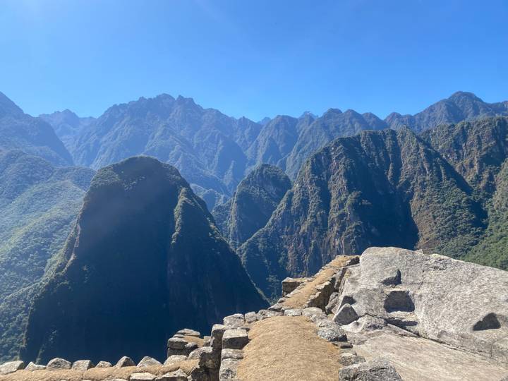 Panoramic Andes mountain spires surrounding Machu Picchu with bright blue sky.