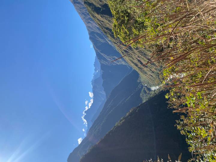 Vertical view down a lush green river valley in the Andes under clear sky.