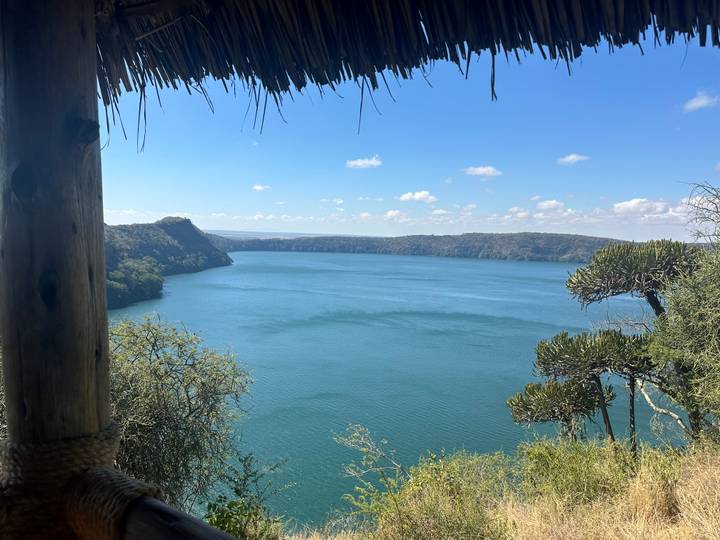Turquoise crater lake viewed from a shaded lodge terrace with thatched roof.