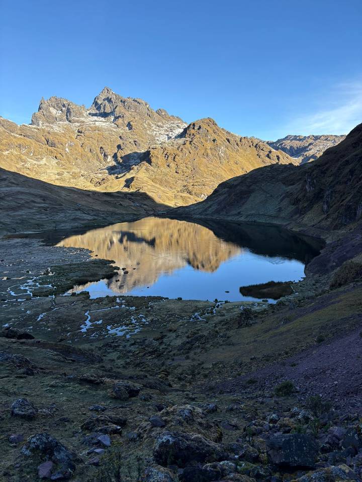 A tranquil alpine lake mirrors surrounding mountains whose slopes glow in warm afternoon light.