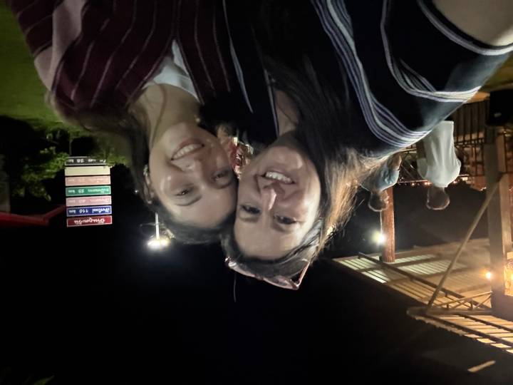 A mother and daughter smile for a selfie under night lights at an open-air venue.