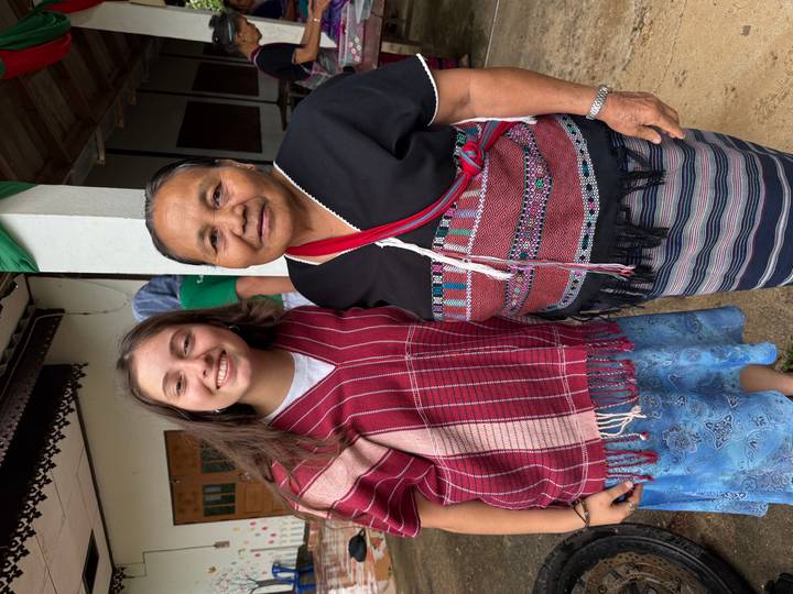 A young traveller and an elder local woman pose together wearing traditional woven garments.