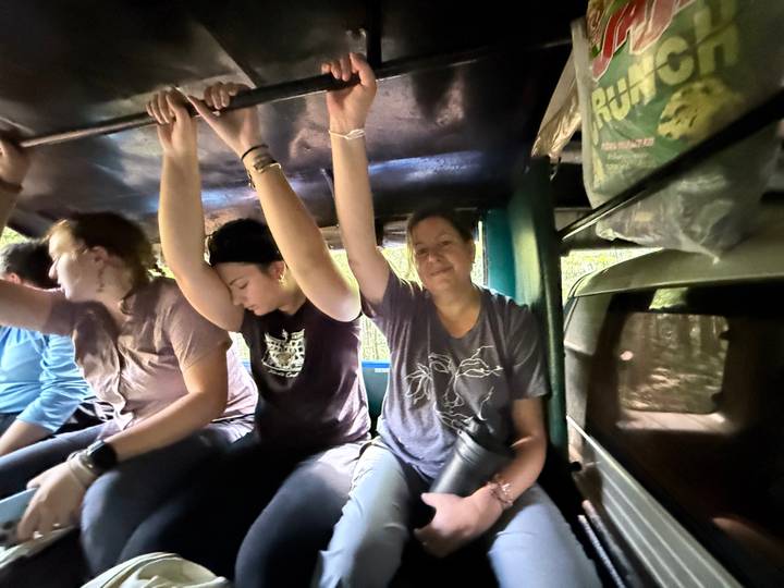 Travellers grip the ceiling rails while riding in the back of an open truck.