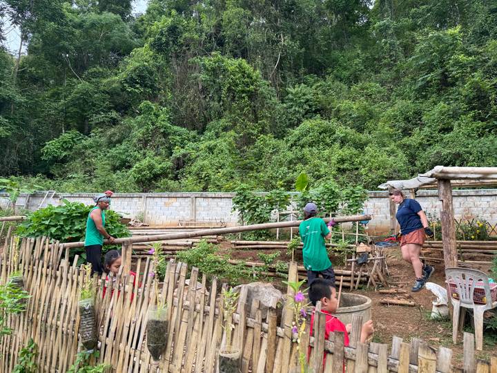 Volunteers work in a terraced garden bordered by bamboo fencing at the edge of dense jungle.