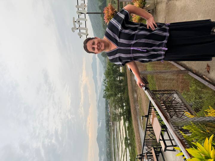 A woman in traditional blouse poses on a balcony overlooking misty rice paddies and distant hills at dawn.