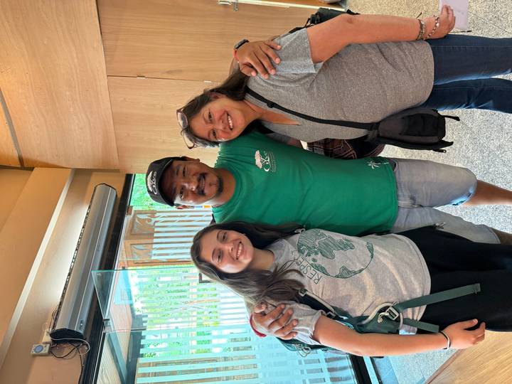 Two travellers hug their smiling local guide inside a modern lobby.