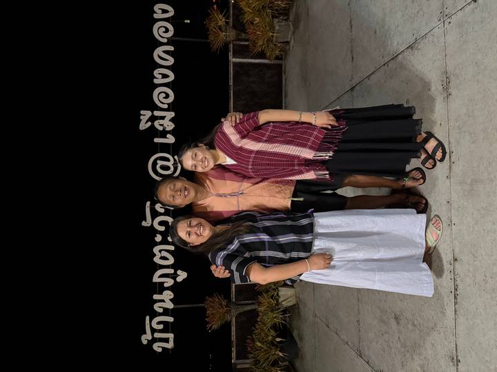 Three travellers pose at night in front of large Thai lettering on a terrace.