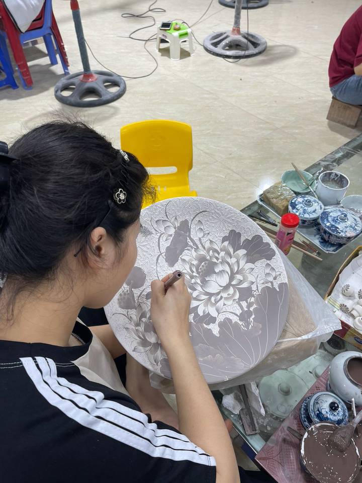 Woman intricately carving floral design on a ceramic plate in an artisan studio