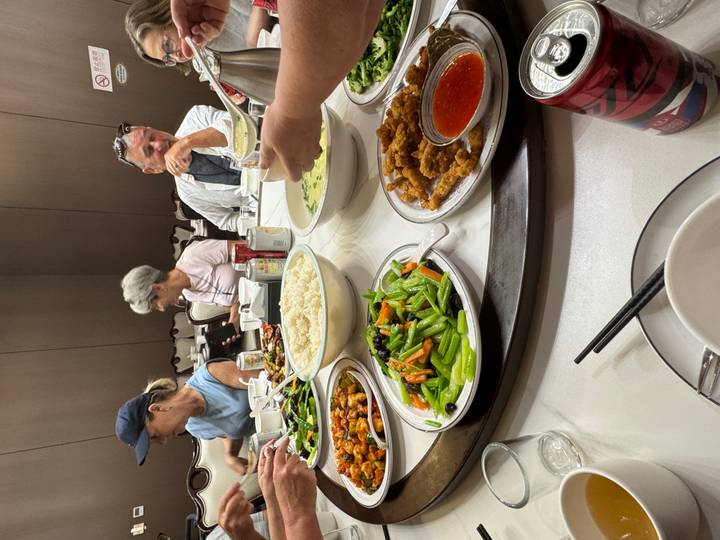 Round restaurant table covered with Chinese dishes as travellers share a meal.