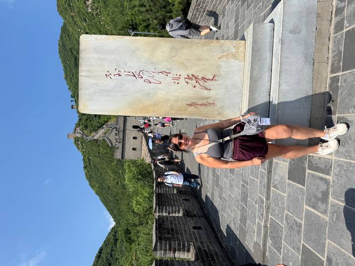 Traveller poses beside an inscribed marble stele on the Great Wall stretching up the mountain.