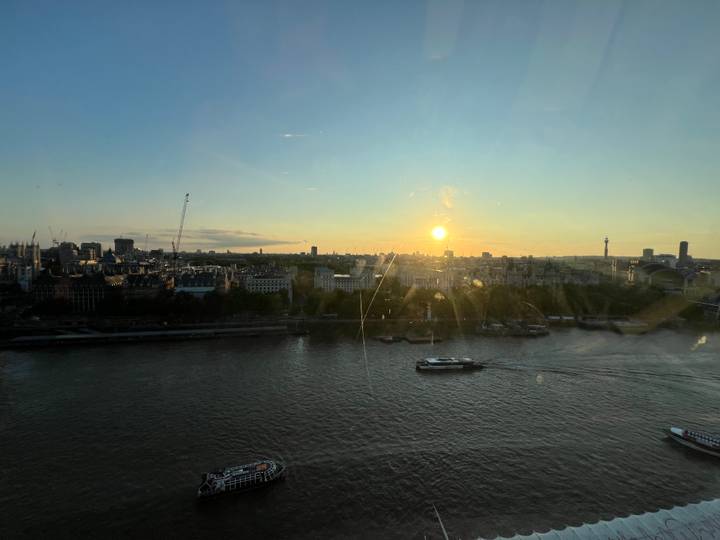 Sunset over the River Thames with city skyline and boats seen through window reflections.