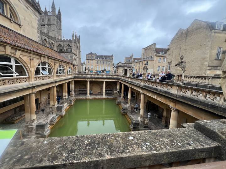 Roman Baths complex with green thermal pool surrounded by classical columns and statues in Bath.