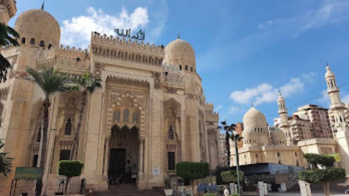 Grand cream-colored mosque with ornate domes and Arabic calligraphy under a bright blue Egyptian sky.