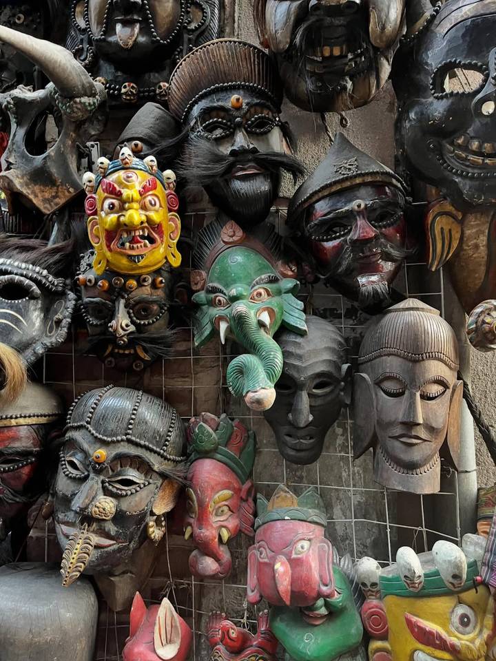 Colorful assortment of traditional Nepali wooden masks displayed on a market wall.