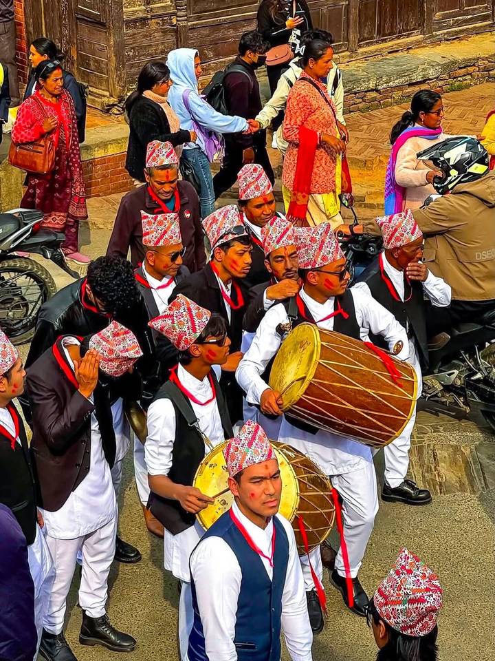 Traditional Nepali musicians in festive attire playing large drums during a street celebration.