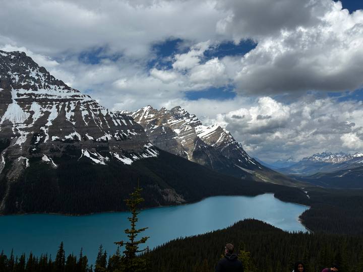 Turquoise Peyto Lake winding beneath rugged snow-dusted mountains under dramatic clouds.
