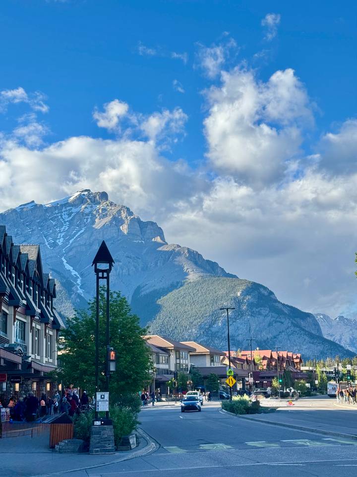 Sunlit Rocky Mountain peak with lingering snow rising behind alpine-style buildings and a small steepled tower.
