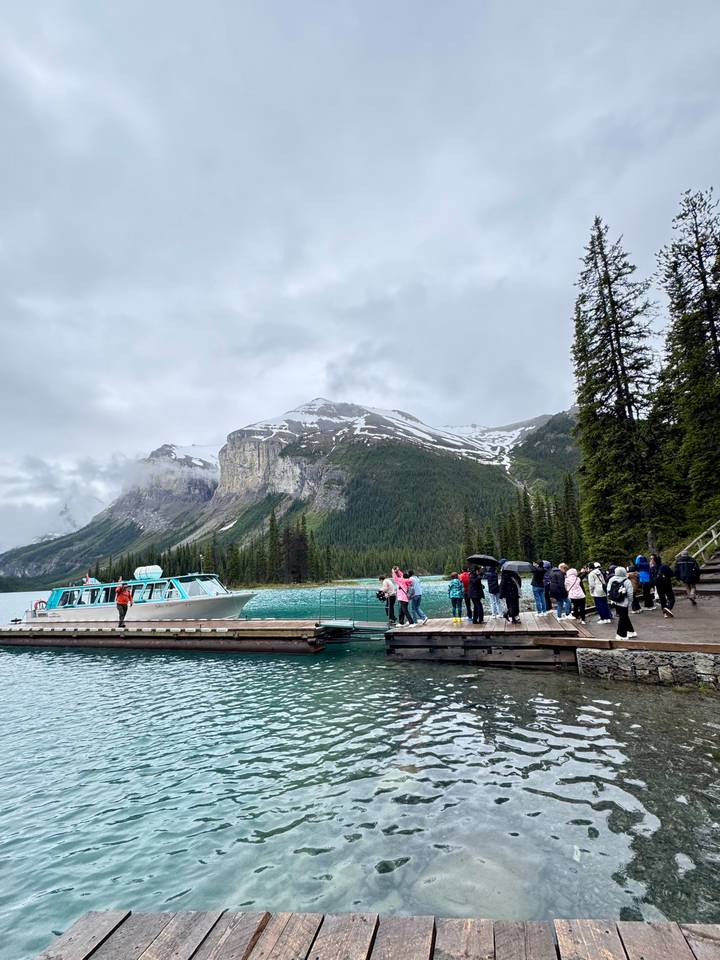 Tour group on a wooden dock boarding a small cruise boat on turquoise glacial lake framed by snow-capped cliffs.