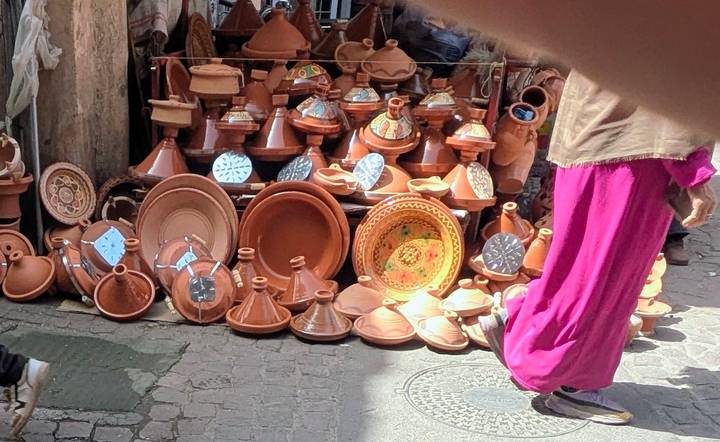 Street stall filled with terracotta tagine pots; partial hand and blurred finger in frame
