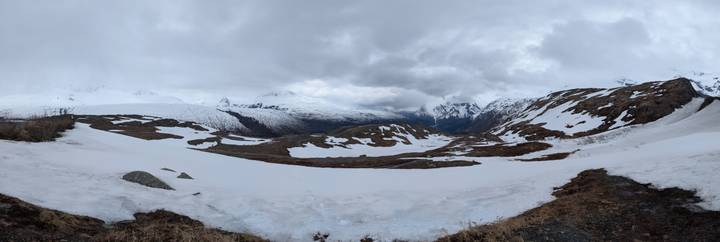 High alpine pass still covered in lingering winter snow beneath dramatic grey skies.