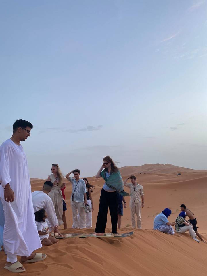 Travellers standing and chatting on rolling desert dunes in the late afternoon light