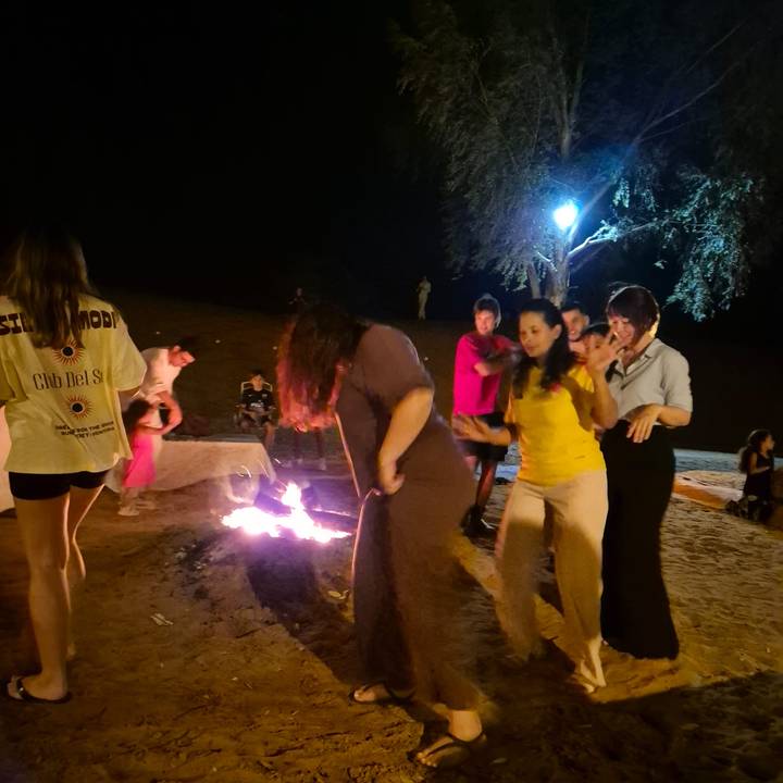 People dancing and socialising around a small campfire at night in the desert