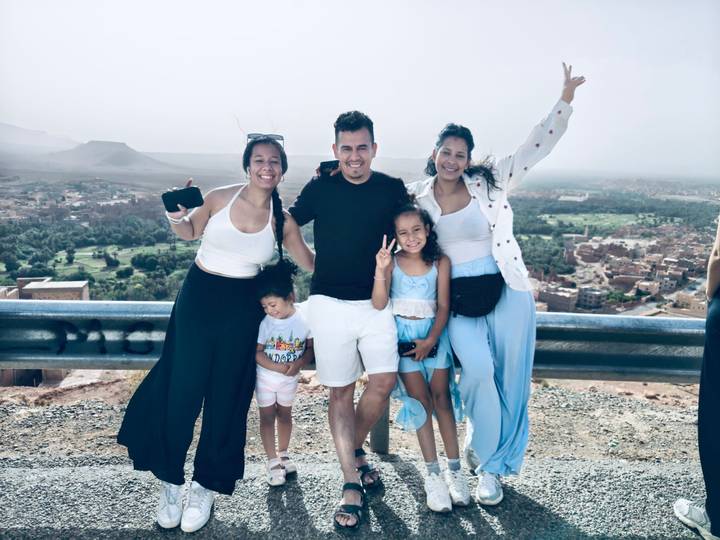 A family poses for a cheerful photo at a hazy mountain viewpoint overlooking a Moroccan valley.