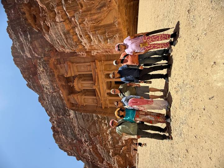 A tour group stands before the iconic Treasury facade carved into the red cliffs of Petra.