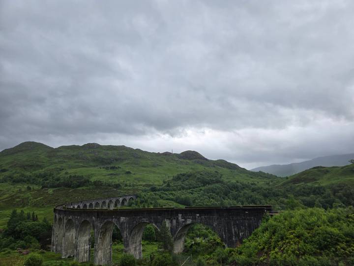 The curving Glenfinnan Viaduct spans a lush green valley beneath thick grey clouds.