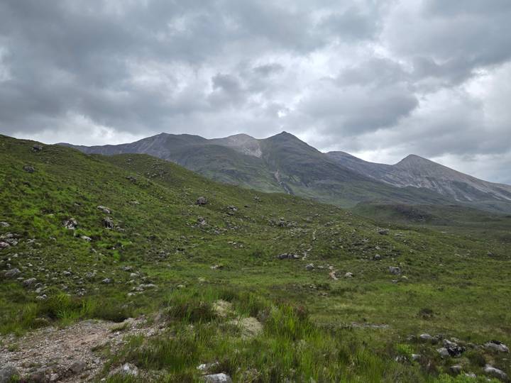 Rolling green moorland leads toward rugged Highland peaks beneath brooding clouds.