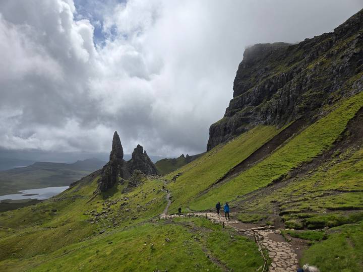 Hikers follow a stony trail toward the dramatic pinnacles of the Old Man of Storr beneath a stormy sky.