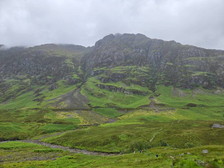 Steep cliff faces draped in emerald vegetation rise above a misty Glencoe valley.