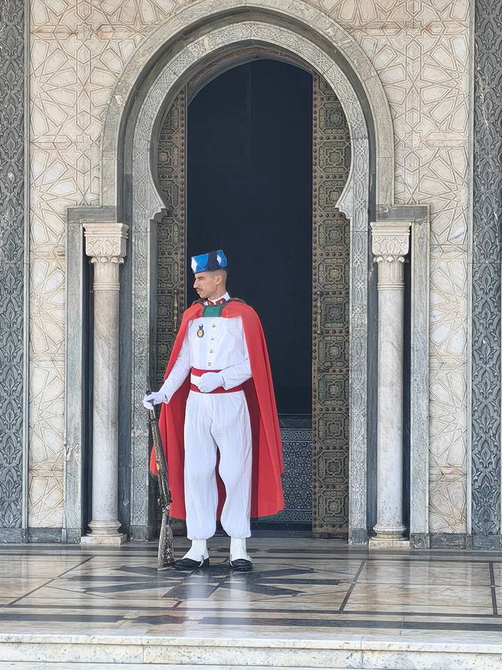 Sentry in white uniform and red cape stands at the ornate marble entrance of the Mausoleum of Mohammed V.
