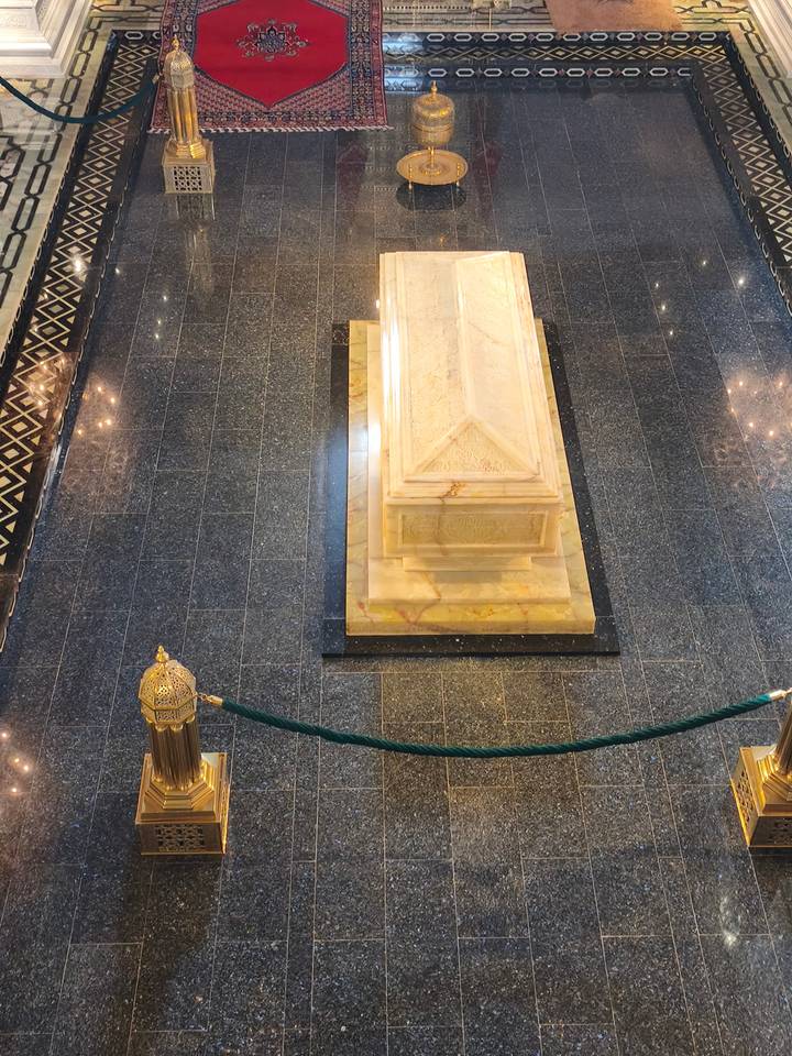 Marble sarcophagus surrounded by polished stone floor and ornate lanterns inside the royal mausoleum.