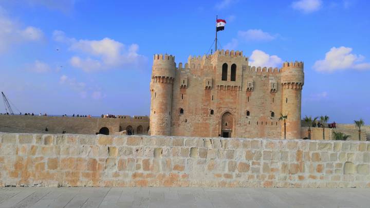 The medieval Citadel of Qaitbay with the Egyptian flag flying against a bright blue sky.
