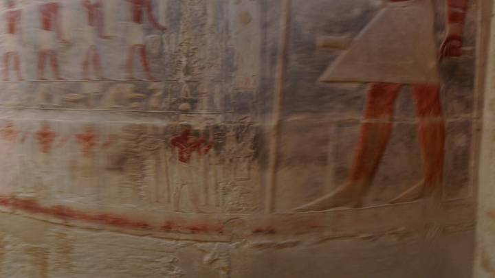 Blurred interior wall showing faint Egyptian reliefs and faded pigment.