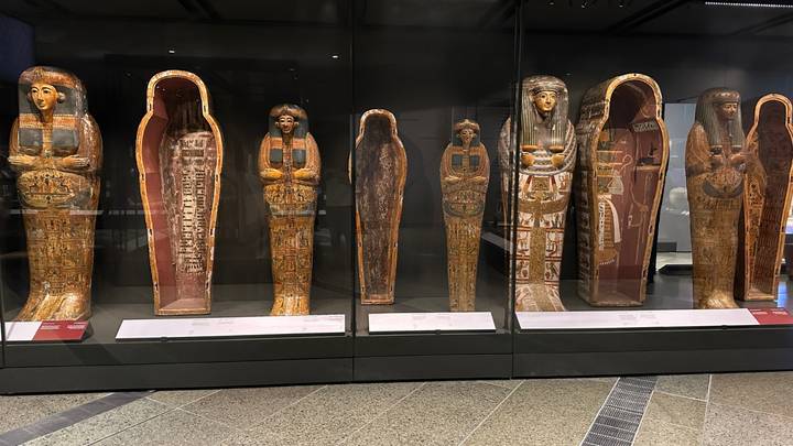 Row of elaborately painted ancient Egyptian coffins on display in a museum case.