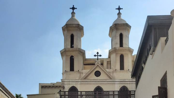 Twin-towered Coptic church façade with crosses rises against a clear blue Cairo sky.