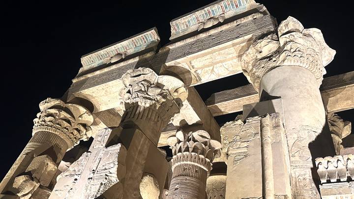 Illuminated stone columns and capitals of Kom Ombo Temple glow against dark night sky.