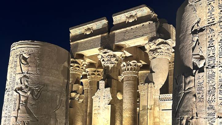 Illuminated sandstone columns and reliefs of an ancient Egyptian temple under a dark night sky.