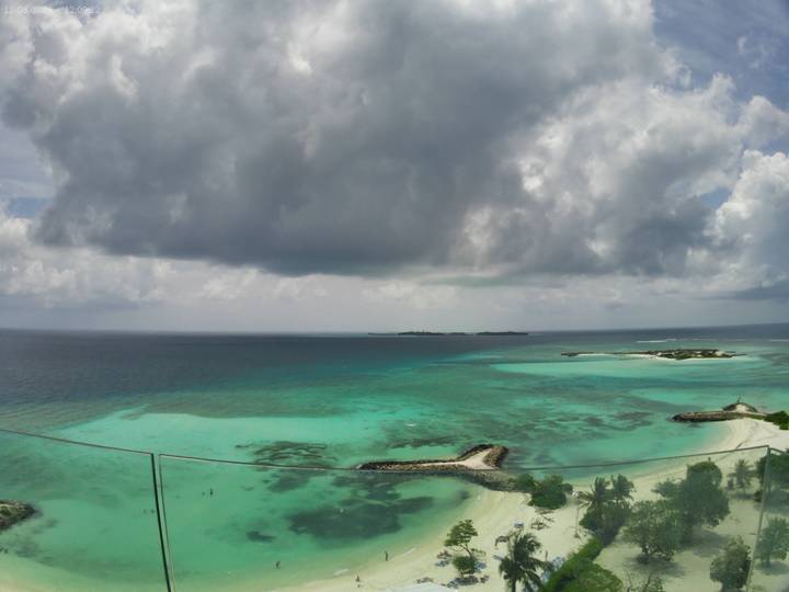A panoramic view of turquoise reefs, sandy islets and deep ocean beneath dramatic storm clouds.