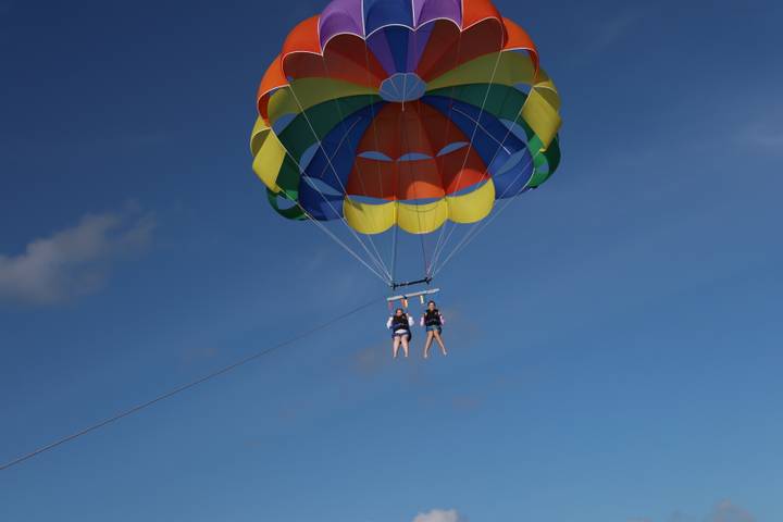 A colorful parasail lifts two thrill-seekers high into a clear blue sky.