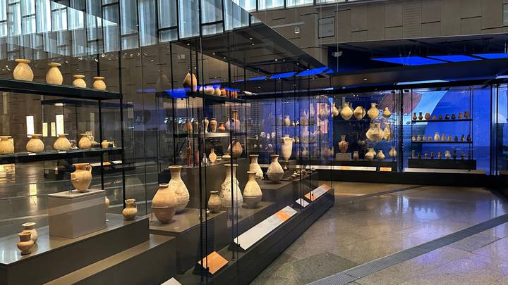 Wide interior shot of museum hall lined with glass cases of ancient pottery under modern lighting.
