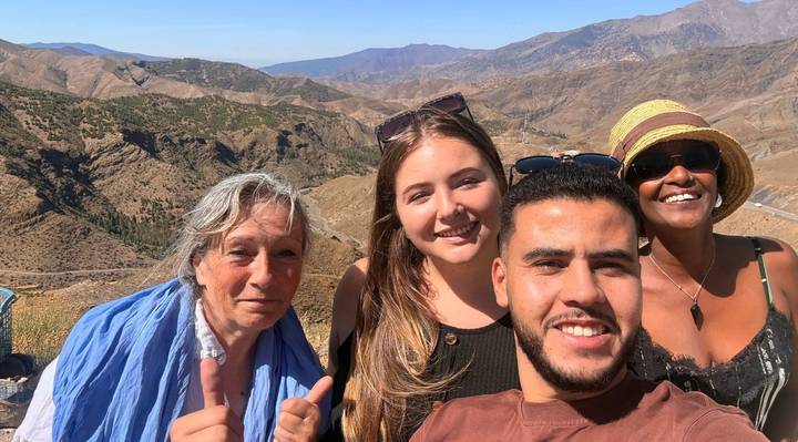 A cheerful group takes a selfie with rolling mountain valleys stretching behind them.