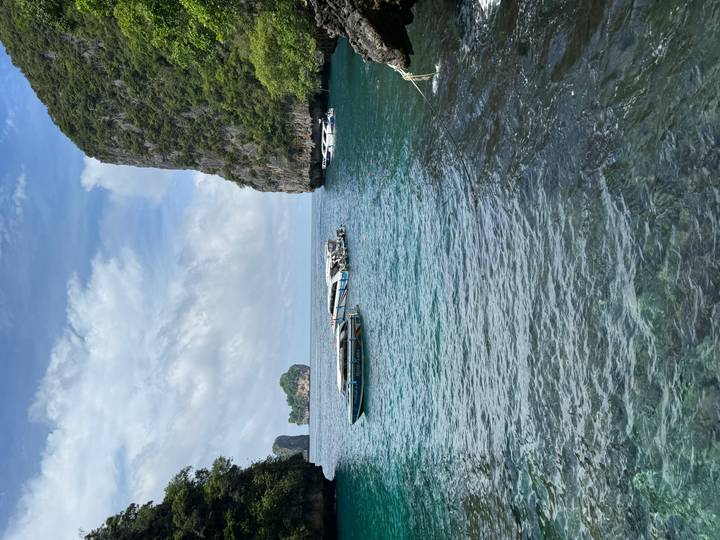 Turquoise sea with anchored speedboats is framed by sheer limestone cliffs and small islands.